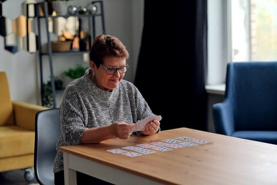 elderly woman playing cards at a table by herself; adjusting to retirement