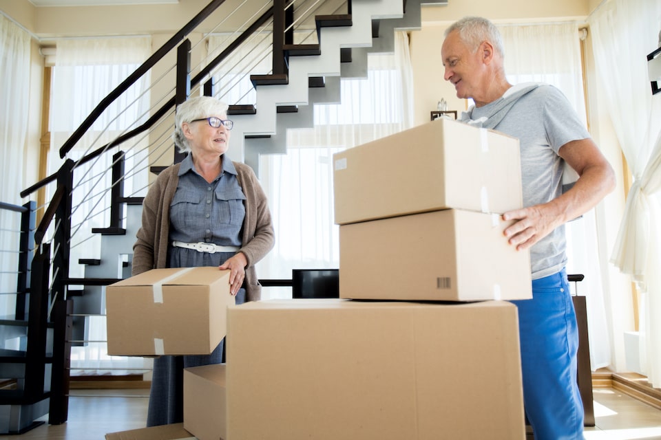 Portrait of happy senior couple packing cardboard boxes while moving to new house; downsizing tips