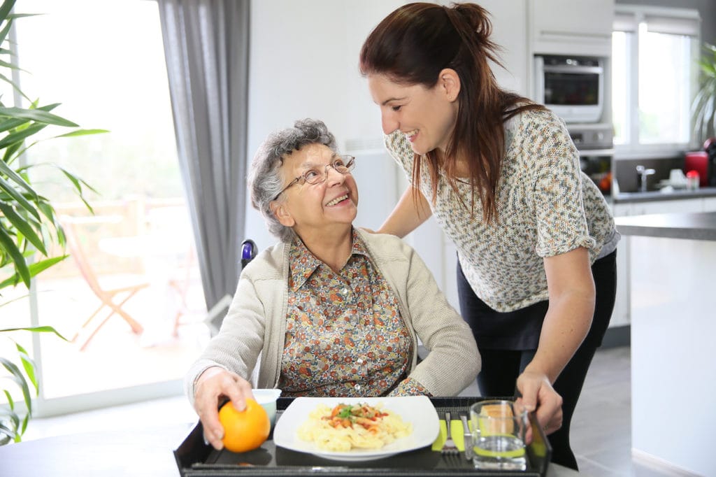 a female volunteer at a nursing home giving food to an elderly resident 