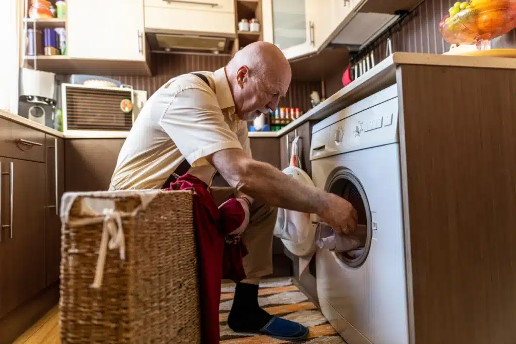 Older man does laundry at his home.