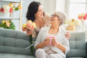 elderly woman at assisted living senior community laughs with niece and accepts flowers