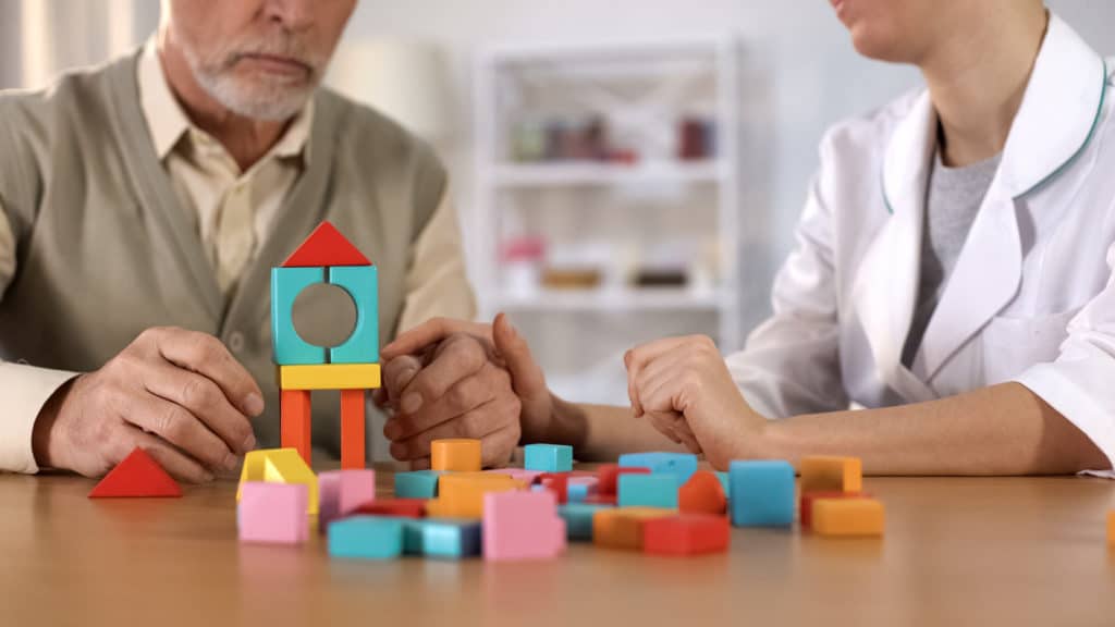 Hospital worker helping dementia patient combine color blocks, brain exercise