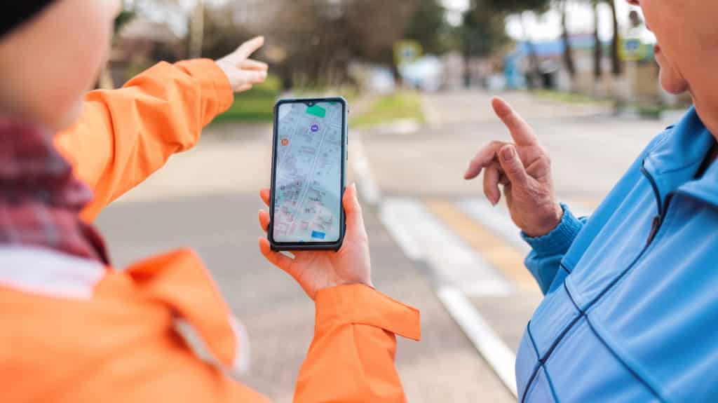 early signs of dementia A woman holds a smartphone with an online map and shows the way to an elderly woman with her hand. Mature woman was lost in the city. Close up. Concept of memory loss and dementia.