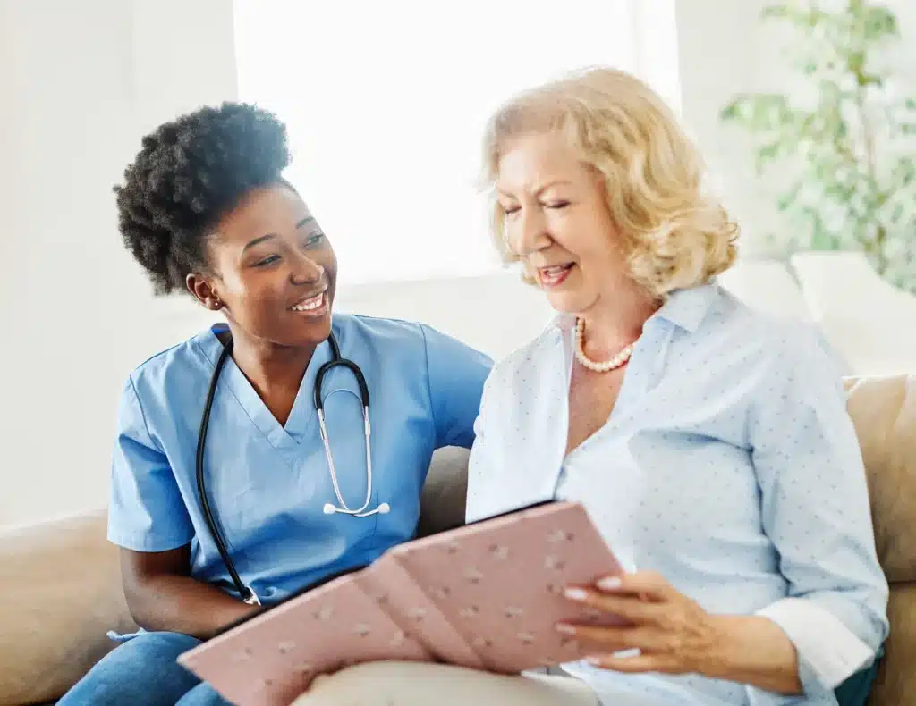 nurse and senior woman sitting at memory care facility and looking at photos