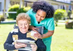 senior sitting on wheel chair and looking at tablet with nurse