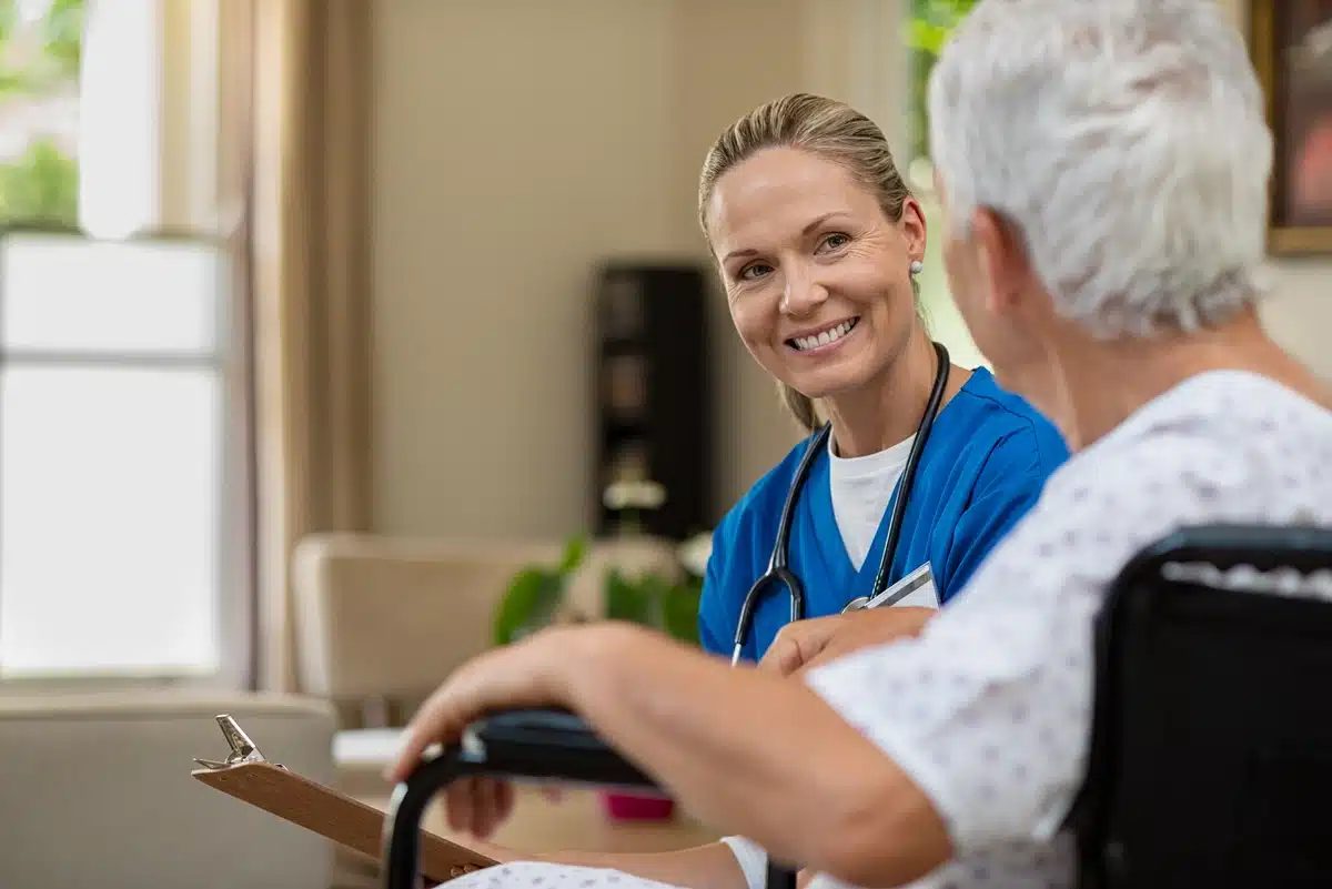 A nurse with a clipboard smiles and listens to elderly patient in wheelchair