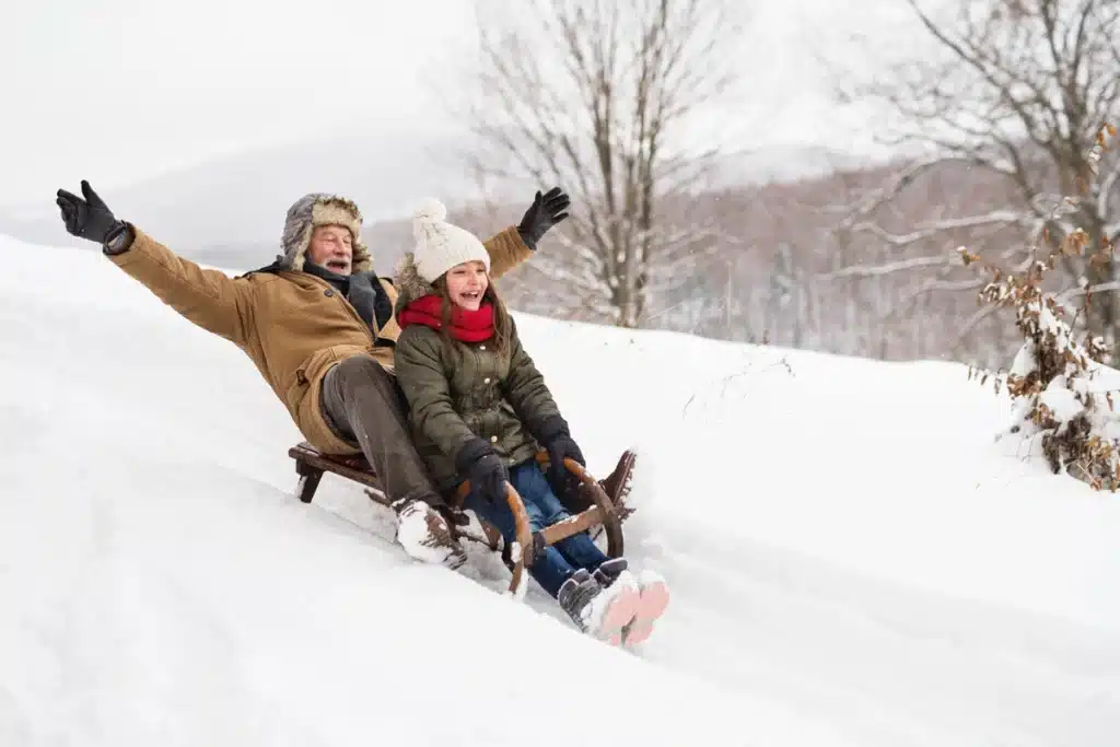 An older man sleds with a young girl
