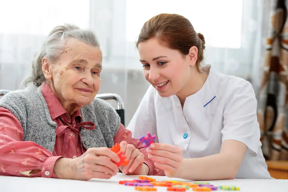 An elderly woman works on a puzzle with a nurse