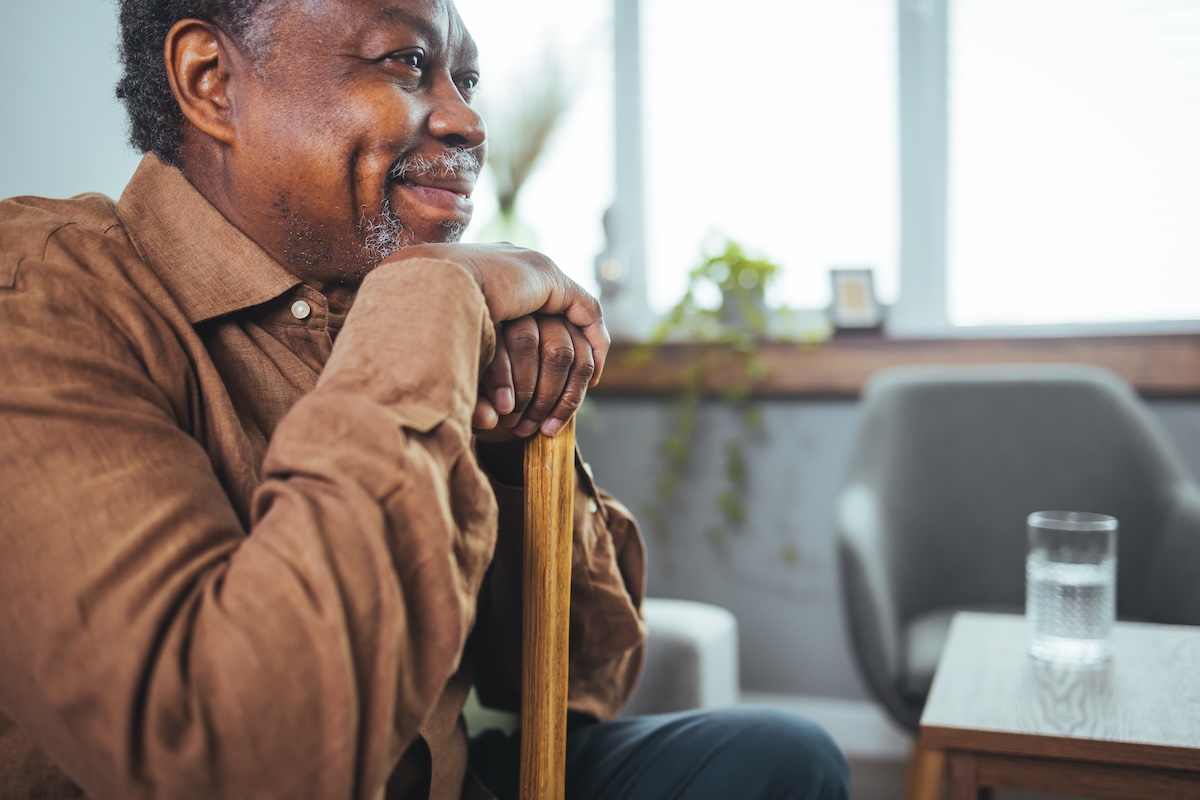 Portrait of a senior man sitting at home with a walking stick.