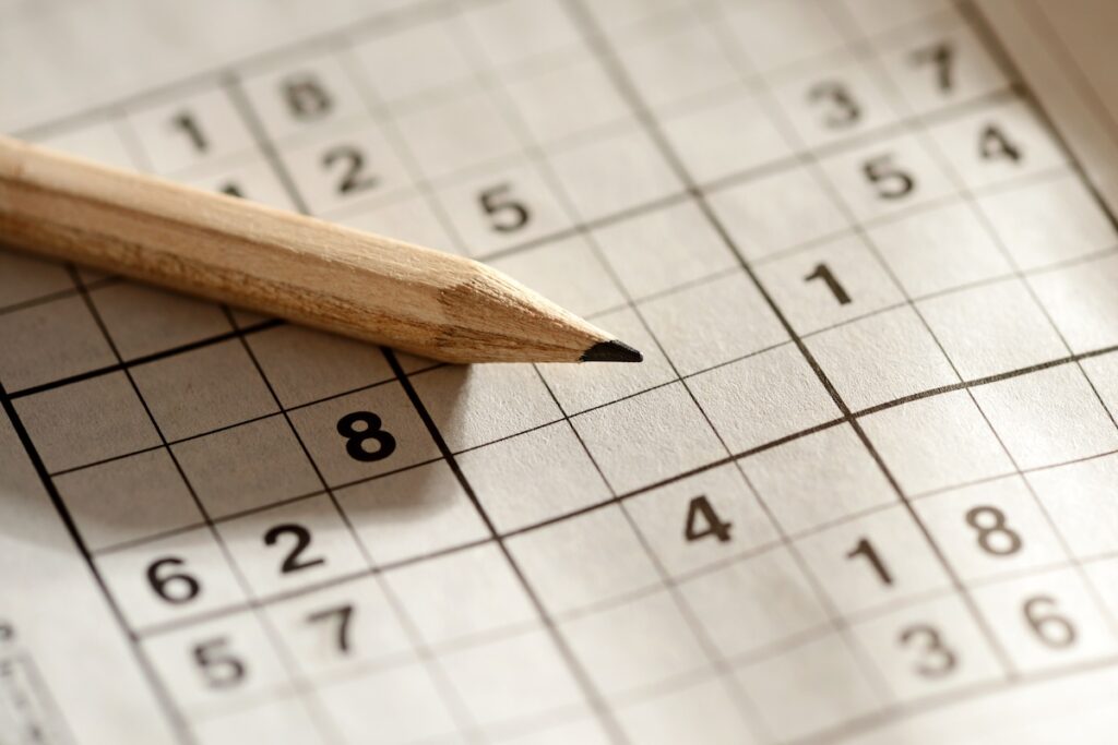 Sharpened wooden pencil lying on a sudoku grid 