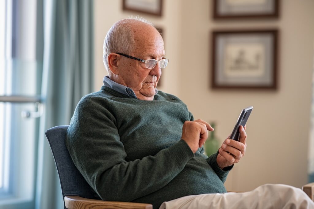 Old man wearing eyeglasses to use smartphone at home